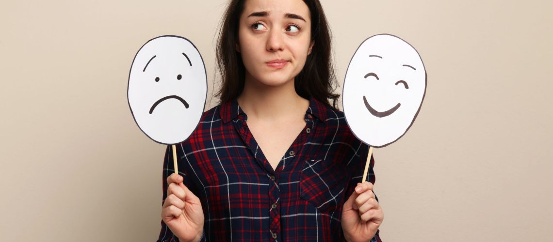Woman with sad and happy paper faces on beige background